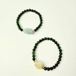 Two beaded bracelets with green and white stones on a beige background