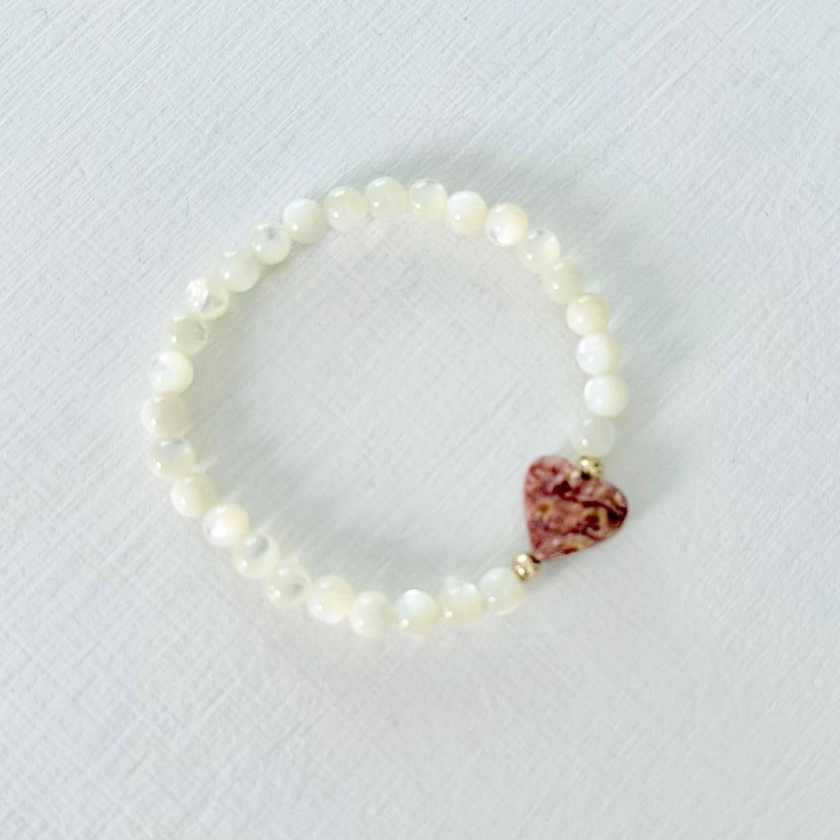 Mother of Pearl bracelet with a heart-shaped shell charm on a light gray background