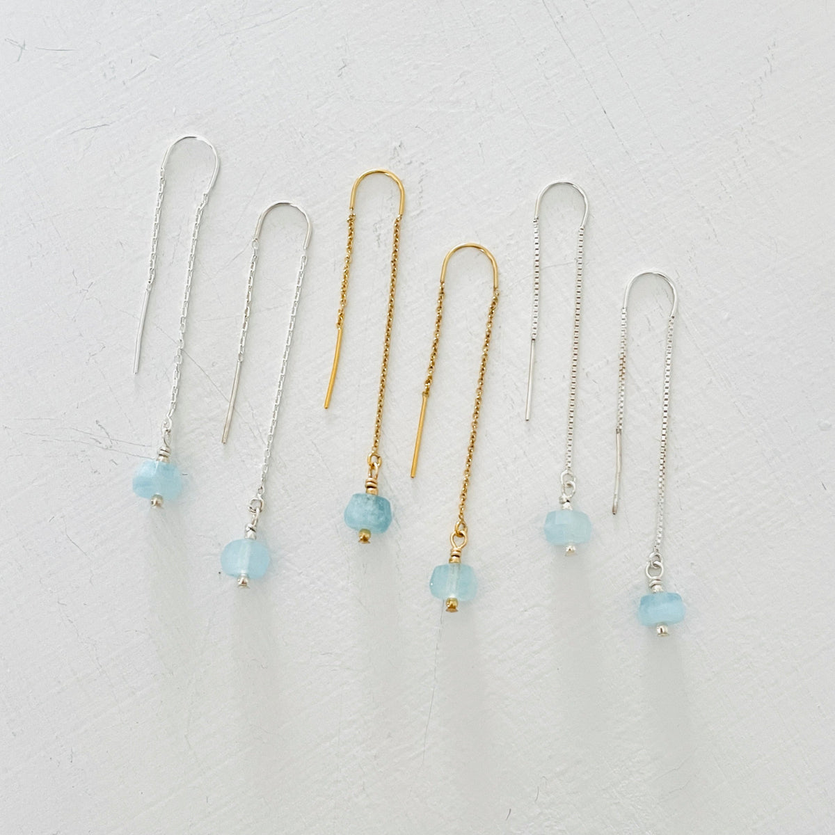 Drop into the Calm Aquamarine Earrings by ZEN by Karen Moore jewelry showing two pairs in sterling silver with a pair in 14K gold in the middle overhead view on white background