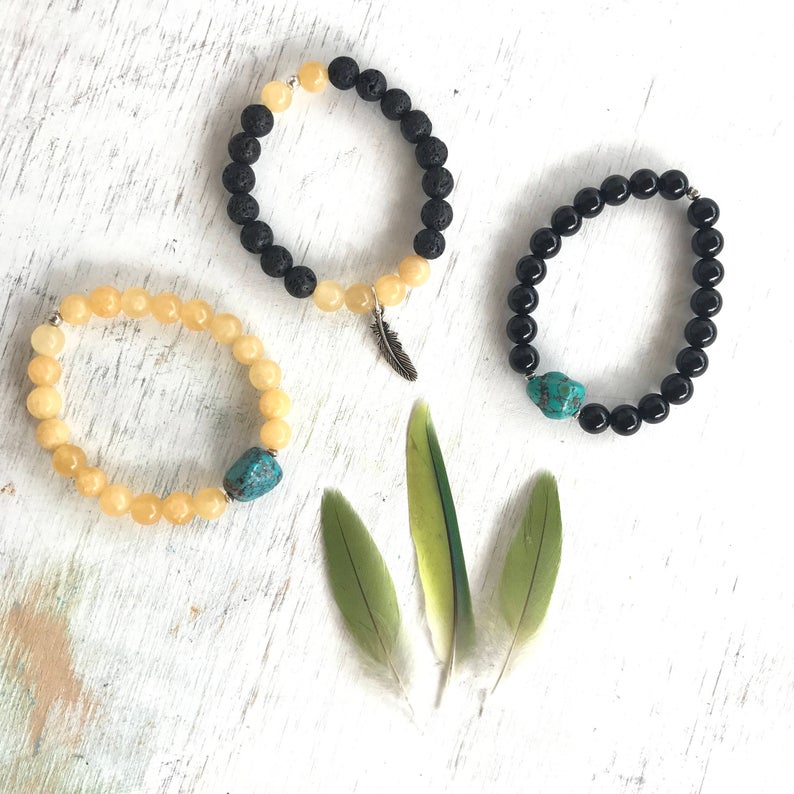 Calcite & lava stone Power Of The Positive Aromatherapy Bracelet by ZEN by Karen Moore shown with two other gemstone bracelets and feathers on white wood